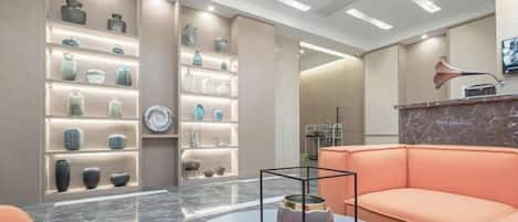 Un hall d’hôtel moderne avec un sol en marbre, un espace salon doté d’un canapé incurvé et un mur orné de vases décoratifs.