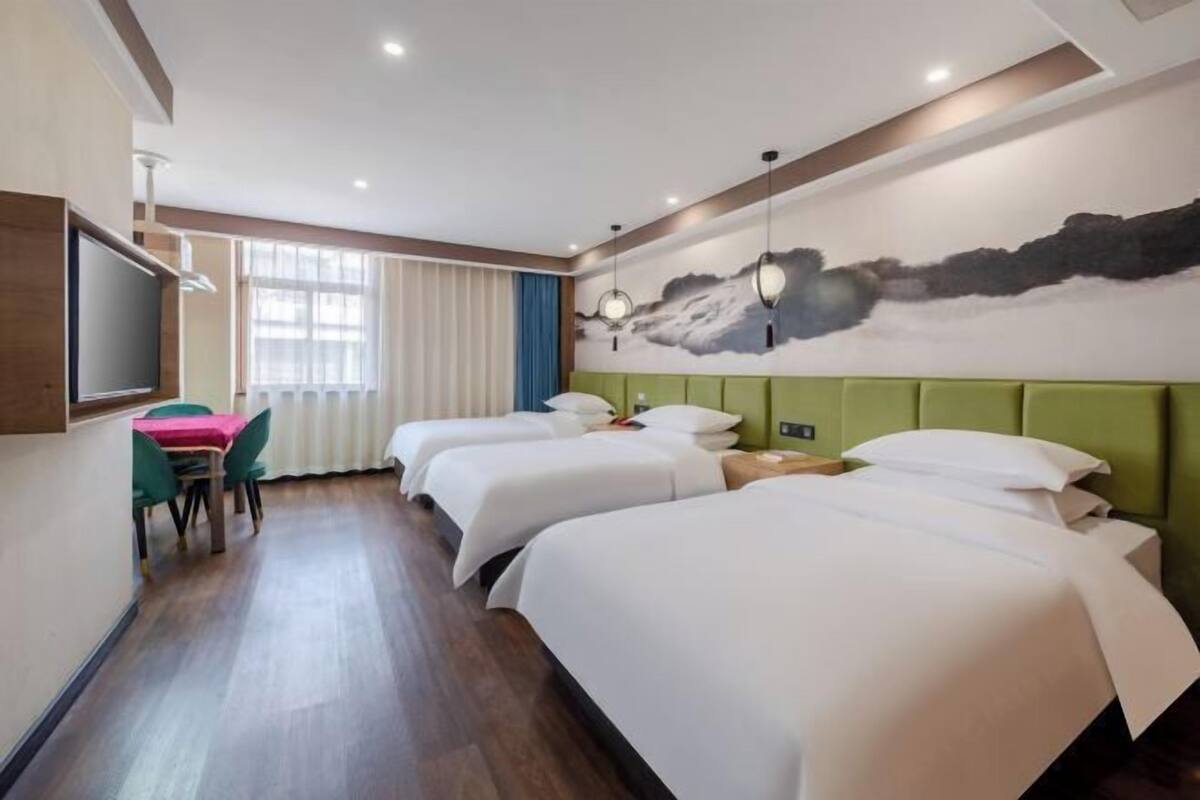 Une chambre d’hôtel avec trois lits, une télévision, une table à manger avec des chaises et un tableau au mur.