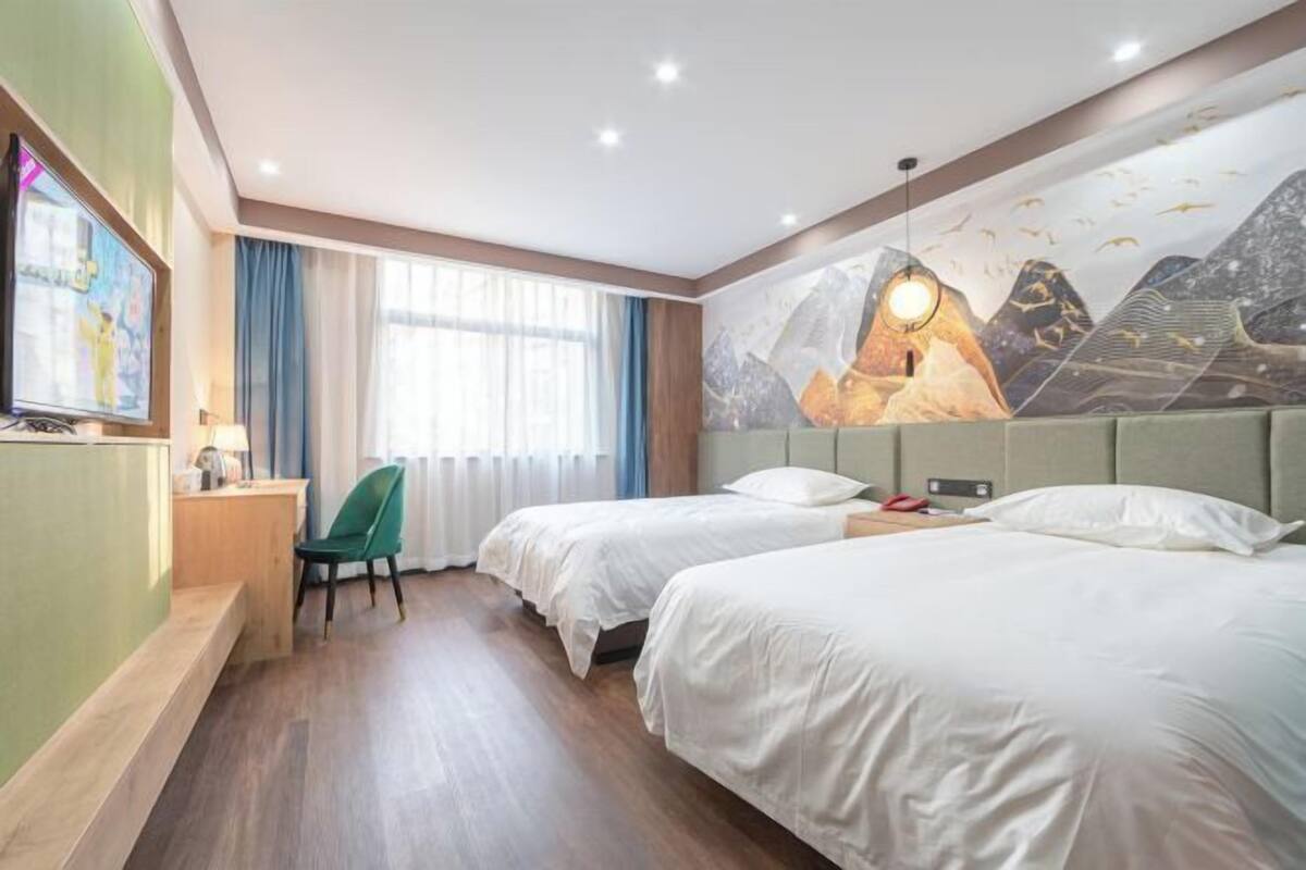 Une chambre d’hôtel avec deux lits, un bureau, une chaise, une télévision et une fresque murale.