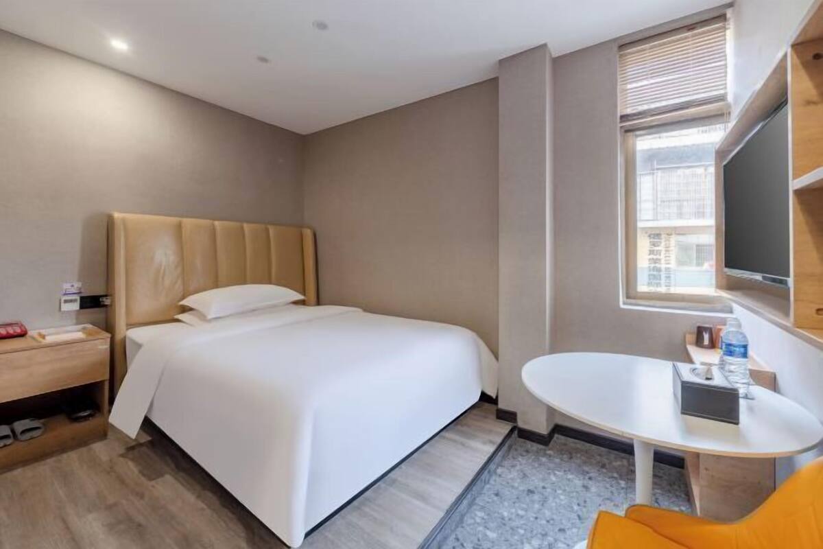 Une chambre d’hôtel avec un lit, une petite table ronde, une chaise, un téléviseur et une fenêtre.