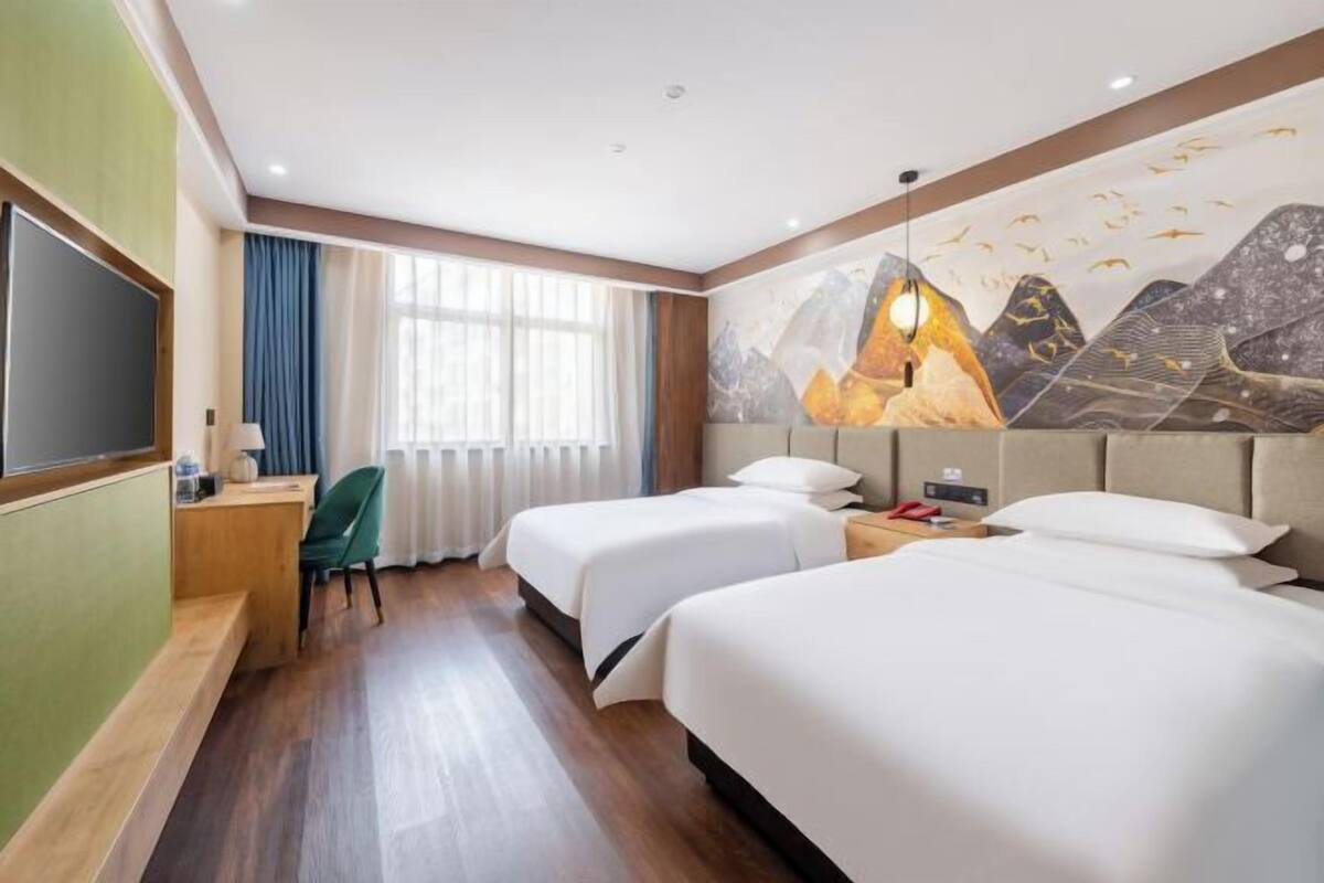 Une chambre d’hôtel avec deux lits, un bureau, une chaise, une télévision et une fresque murale.