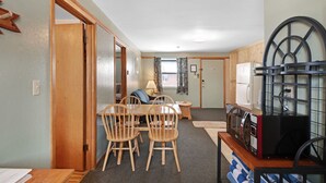 A compact kitchen with wooden chairs, a dining table, and a microwave on a wooden counter.