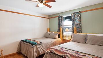 A bedroom with two single beds, a ceiling fan, wooden headboard, and a window with patterned curtains.