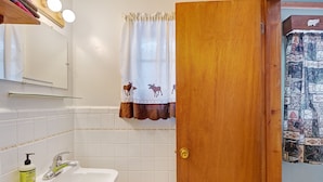 A bathroom with a white sink, a mirror, and a shower curtain with a moose pattern. - Foothills Lodge 3 - South Fork (South Fork)