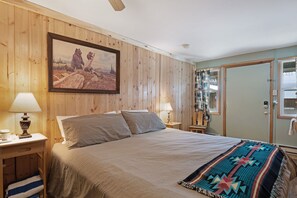 Ein Schlafzimmer mit Holzvertäfelung, einem Bett, zwei Nachttischlampen, einem gerahmten Bild und einer Tür mit Spiegel.