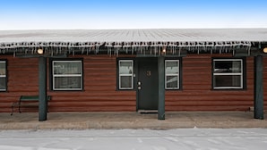 A wooden cabin with a dark green door and windows, a bench outside, and icicles hanging from the roof. - Foothills Lodge 3 - South Fork (South Fork)