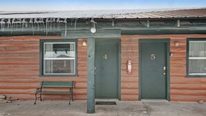 Una cabaña de troncos con dos puertas, numeradas 4 y 5, y un banco afuera.
