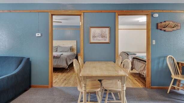 Una habitación con una mesa de comedor de madera, dos sillas, un sofá y una cama con cabecera.