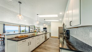 A modern kitchen with white cabinets, a black countertop, and a view to the sea. - Oceanfront, Hot Tub, Sleeps 23-62! (Waldport)