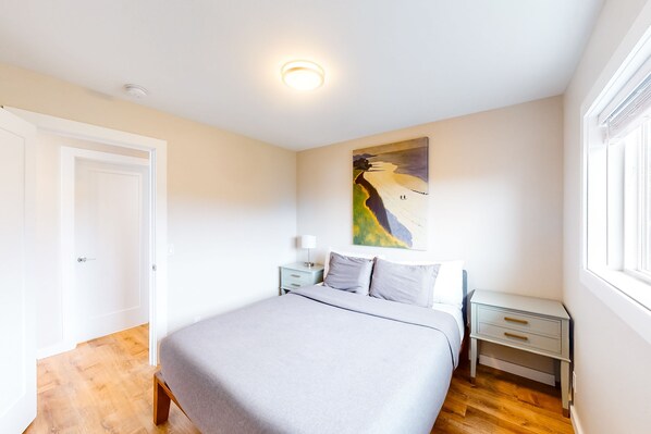 A bedroom with a bed, nightstands, a painting, and a window.