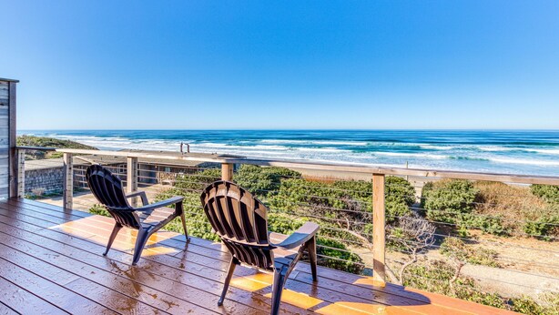 Una terraza de madera con dos sillas Adirondack con vista a una playa y olas.