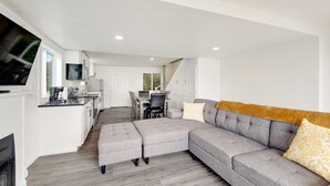 Un salon moderne avec un canapé d’angle gris, des poufs et un téléviseur à écran plat.