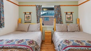 A twin bedroom with two beds, a wooden nightstand, and a window with curtains.