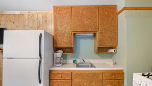 A compact kitchen with wooden cabinets, a white refrigerator, a coffee maker, and a sink.