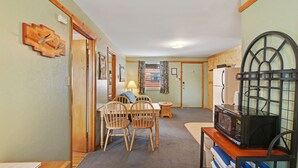 A compact kitchen with a microwave, wooden chairs, a small dining table, and a door leading to another room.