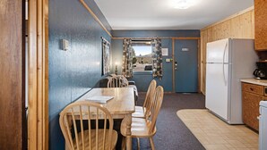 Une cuisine compacte équipée d’un réfrigérateur, de meubles de rangement en bois et d’un coin repas avec des chaises et une table.