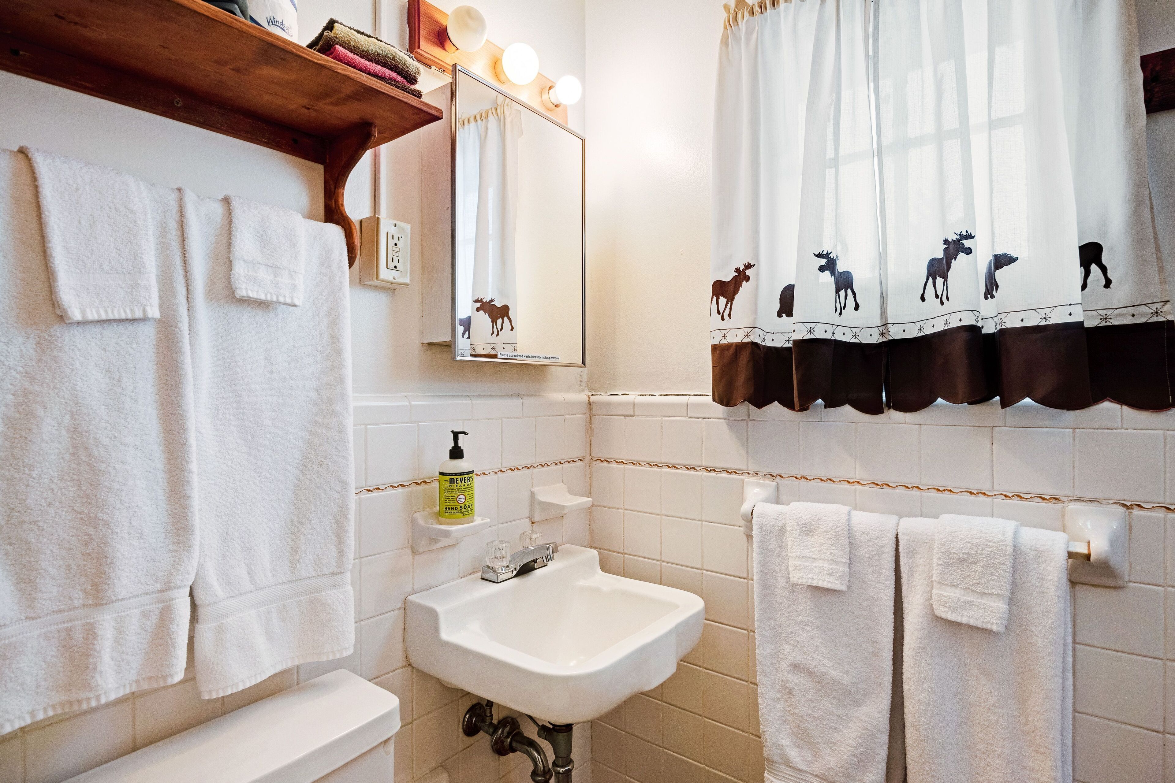 A bathroom with white tiles, a sink, a mirror, and towels.