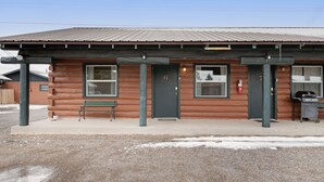 Une cabane en rondins avec une pancarte portant le numéro 6, un banc et un barbecue à l’extérieur.