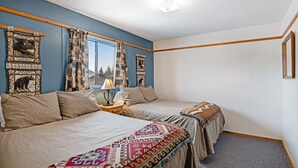 Une chambre avec deux lits, une fenêtre ornée de rideaux à motifs, une table de chevet avec une lampe et un mur décoré de tableaux encadrés.