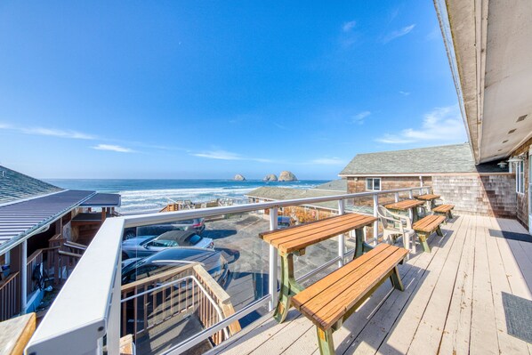 A deck with wooden benches overlooking a beach with parked cars and a view of the ocean.