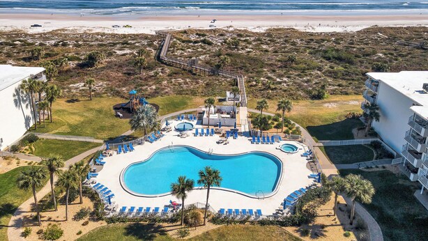 A resort with a central swimming pool, a beach, and a boardwalk.