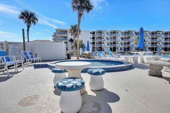 Un espace aménagé au bord de la piscine, avec des chaises longues, une piscine et un bâtiment doté de balcons en arrière-plan.