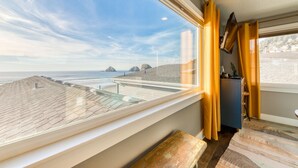 A room with a large window overlooking a beach, a wooden bench, and a small table with a plant. - Oceanside Inn #6: Pet-free unit. No pets allowed. (Oceanside)