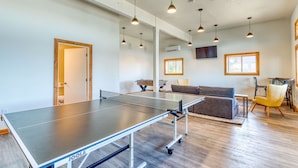 A ping pong table in a modern living room with a sofa, a yellow chair, and a TV mounted on the wall. - Cape Cod Cottages #7 - Oceanfront with Fireplace! (Waldport)