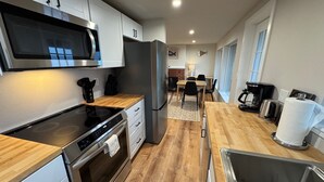 A modern kitchen with stainless steel appliances, a wooden countertop, and a dining area with a table and chairs. - Cape Cod Cottages #7 - Oceanfront with Fireplace! (Waldport)