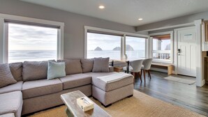 A modern living room with a sectional sofa, a coffee table, and a view of the ocean through large windows. - Oceanside Inn 1: Pet-free unit. No pets allowed. (Oceanside)