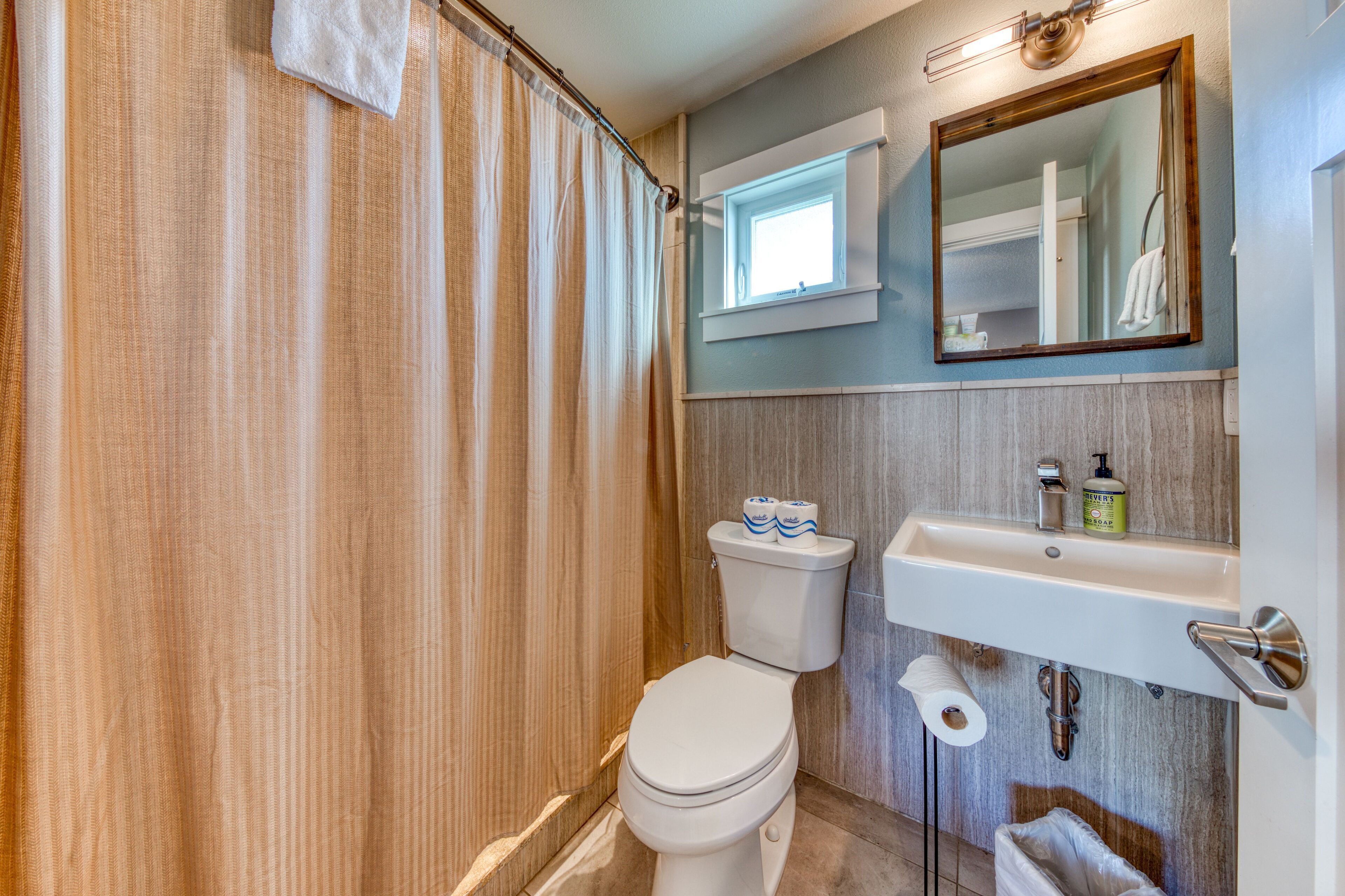 Un baño con inodoro, lavamanos, espejo y cortina de ducha.
