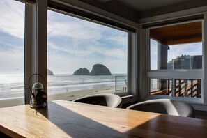 A room with a view of the beach and ocean, a wooden table, and a chair.