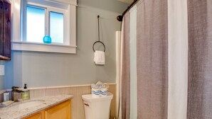 Et badeværelse med toilet, vask, et vindue med en vase og en bruseforhæng.