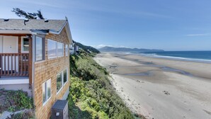 A coastal house with a balcony overlooking a beach.