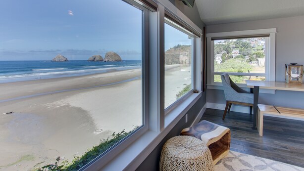 A modern room with large windows overlooking a beach, a wooden bench, and a dining area.