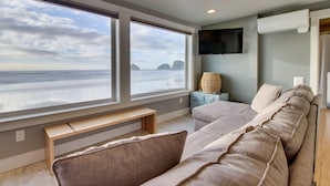 A modern living room with a large window overlooking the sea, a flat-screen TV mounted on the wall, and a comfortable sofa. - Oceanside Inn #4: Pet-free unit. No pets allowed. (Oceanside)