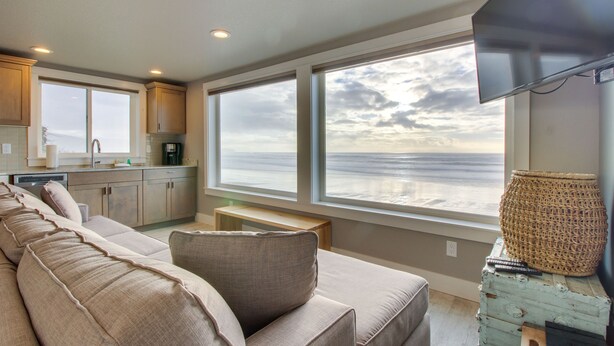 A modern living room with a large window overlooking the ocean, a sofa, a coffee table, and a television. - Oceanside Inn #4: Pet-free unit. No pets allowed. (Oceanside)