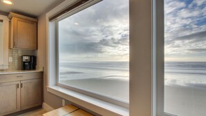A kitchen with wooden cabinets, a countertop, and a view of the beach through a large window. - Oceanside Inn #4: Pet-free unit. No pets allowed. (Oceanside)