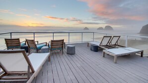 A wooden deck with lounge chairs and a table, overlooking a calm sea and distant islands during sunset. - Oceanside Inn #4: Pet-free unit. No pets allowed. (Oceanside)