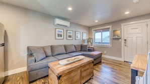 A modern living room with a gray sectional sofa, a wooden chest of drawers, and a window with a view.