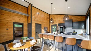A modern kitchen with wooden walls, a central island with bar stools, and a dining area with a round table and chairs. - Couples ONLY + Spa Suite + Hot Tub + 3 Fireplaces - Escape to Whiskey Nights (Broken Bow)