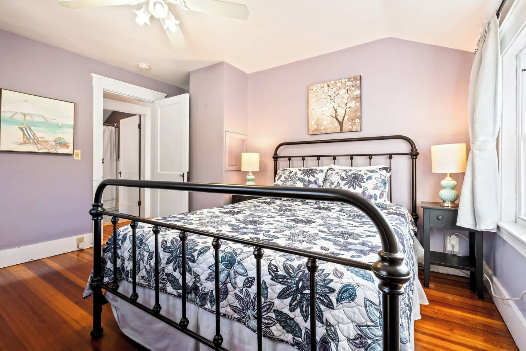 A bedroom with a bed, a nightstand, a lamp, a painting, and a door.