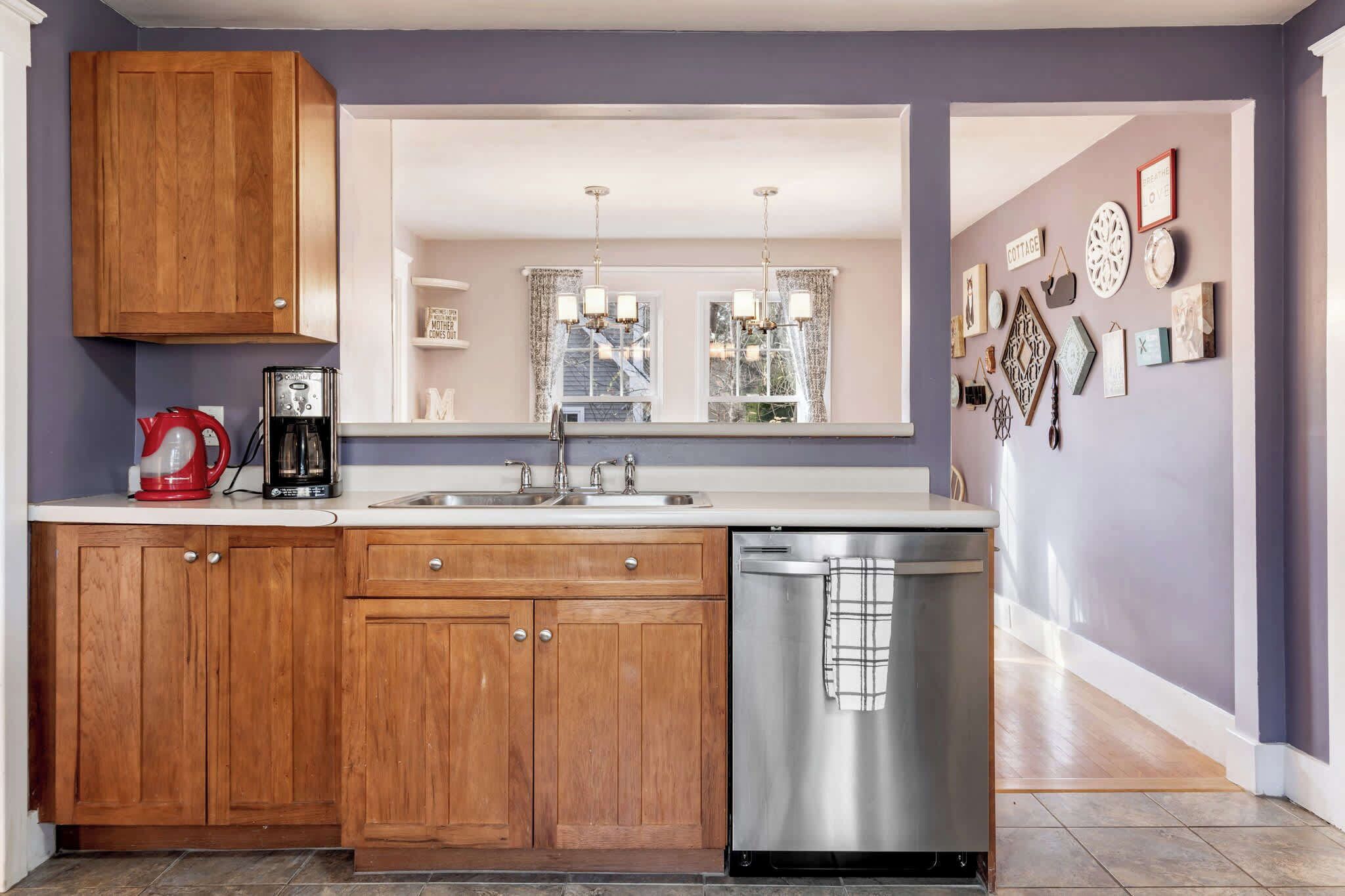 Una cocina moderna con armarios de madera, lavavajillas de acero inoxidable y un amplio ventanal con cortinas.