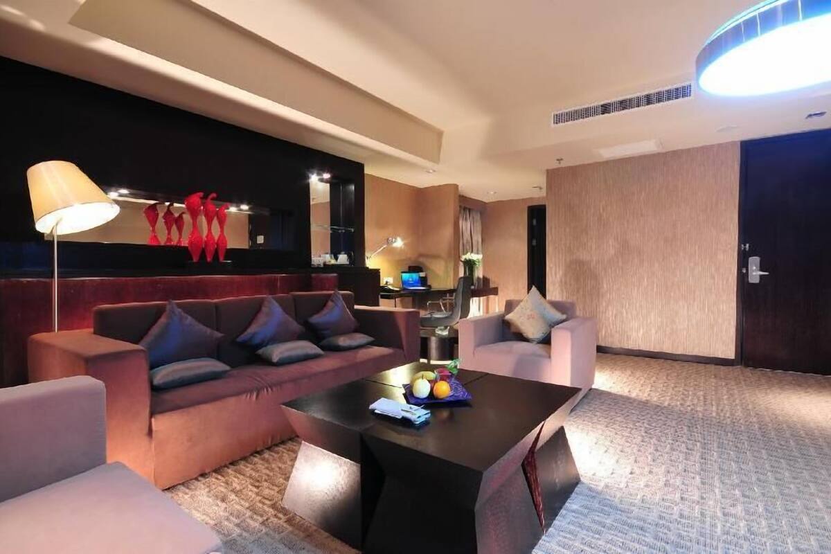 Una habitación de hotel moderna con sofá, sillones, una mesa de centro y una lámpara.