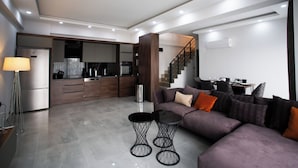 A modern living room with a sectional sofa, a coffee table, and a dining area with a kitchen in the background. - Living Dream Duplex Belek (Antalya)