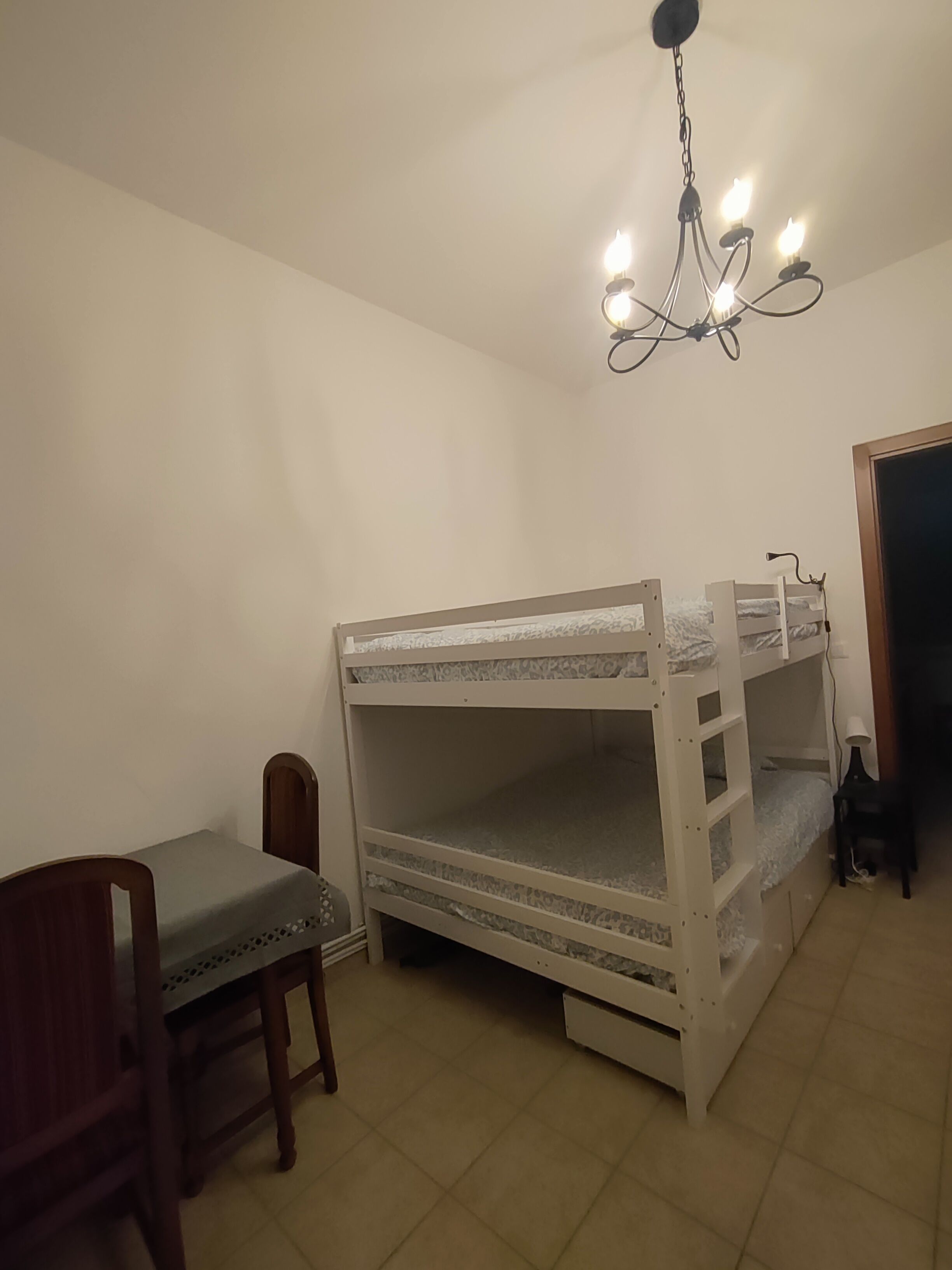 A bunk bed room with a desk and chair, a chandelier, and a door.