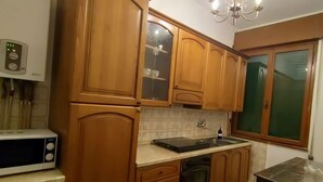 A kitchen with wooden cabinets, a microwave, a sink, and a chandelier. - Cozy house in the Po Delta Park near the sea Belemi's House (Ca' Venier)
