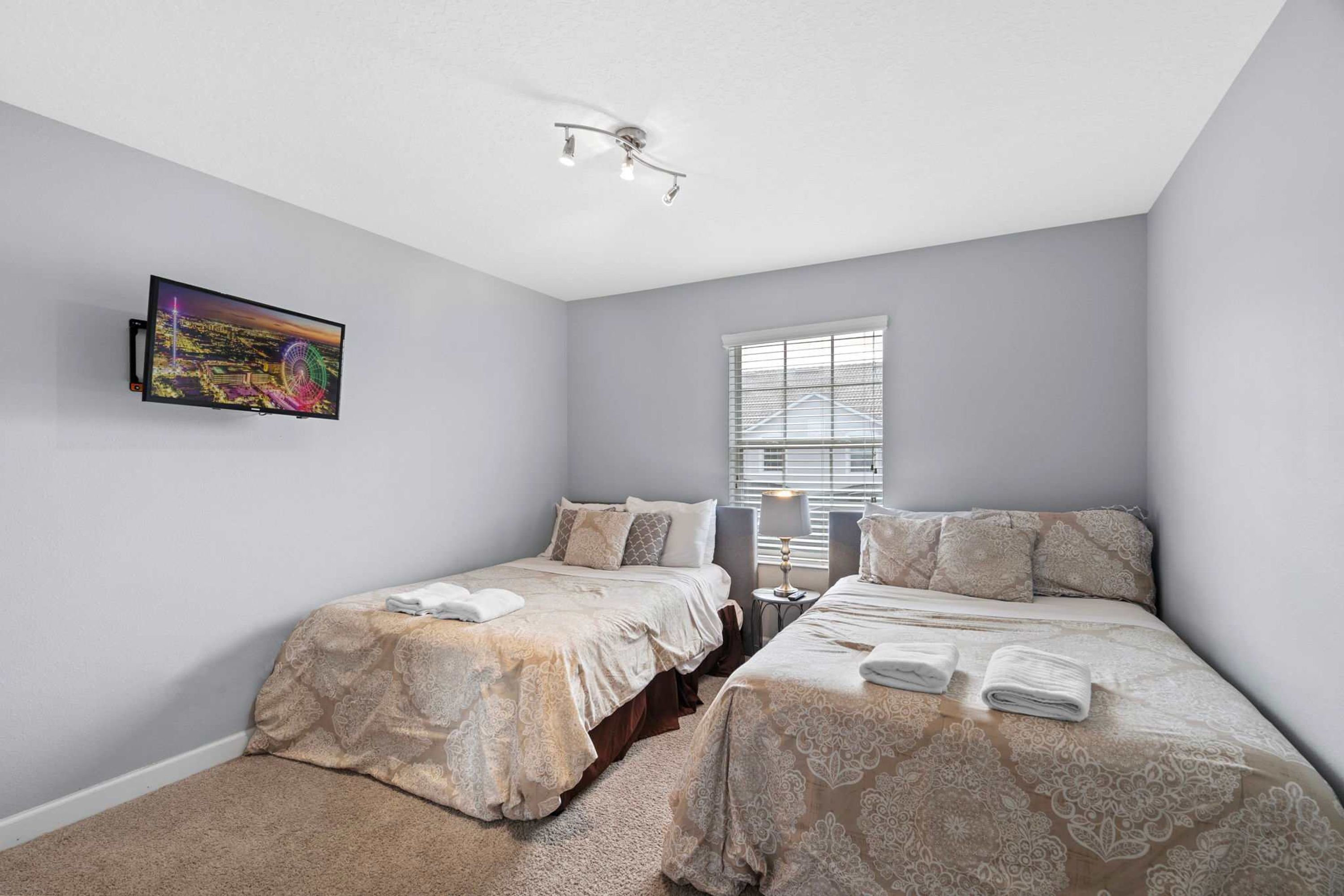 A bedroom with two beds, a ceiling fan, a window with blinds, and a painting on the wall.