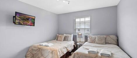 A bedroom with two beds, a ceiling fan, a window with blinds, and a painting on the wall.