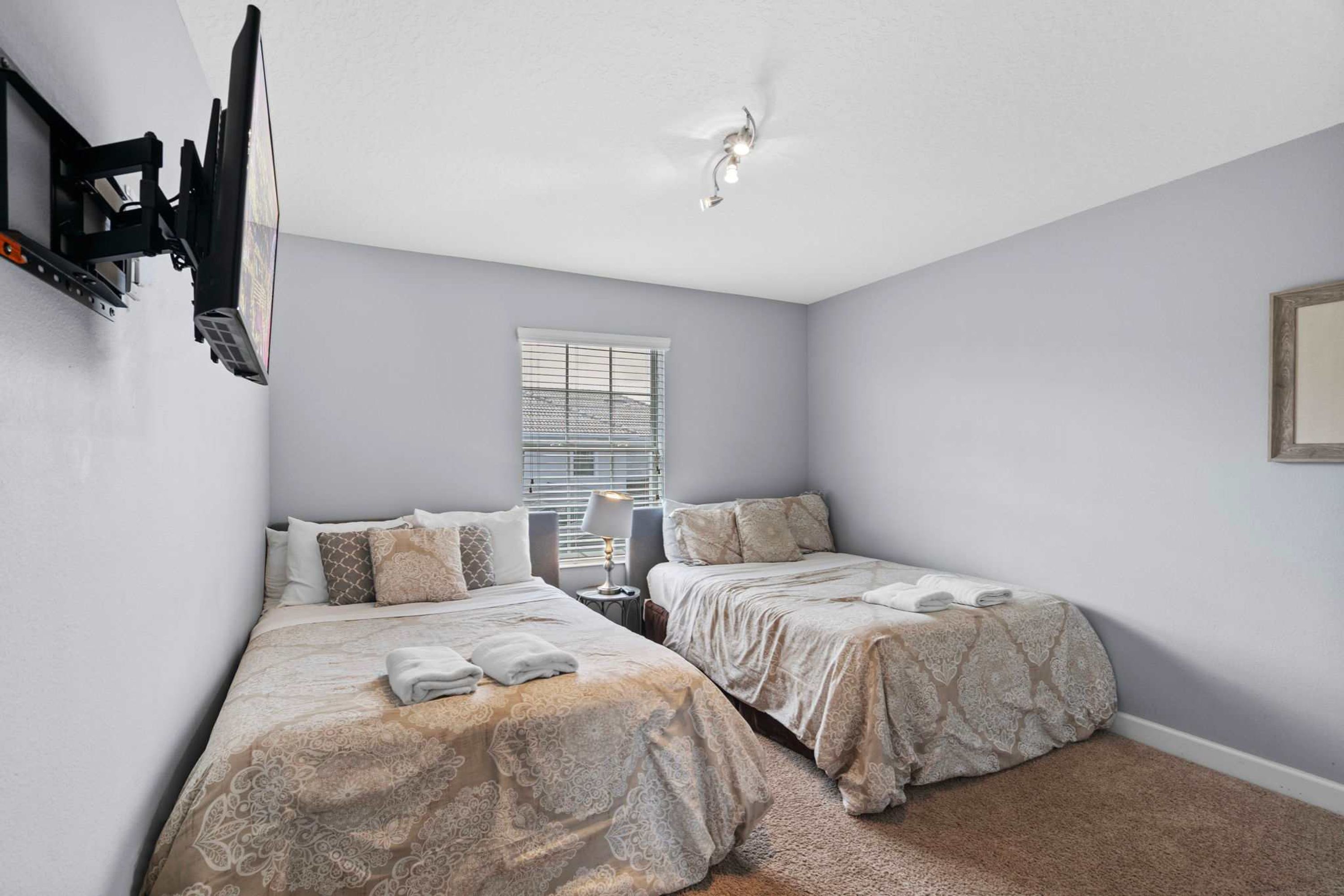 A bedroom with two beds, a ceiling fan, a window with blinds, and a lamp on a bedside table.
